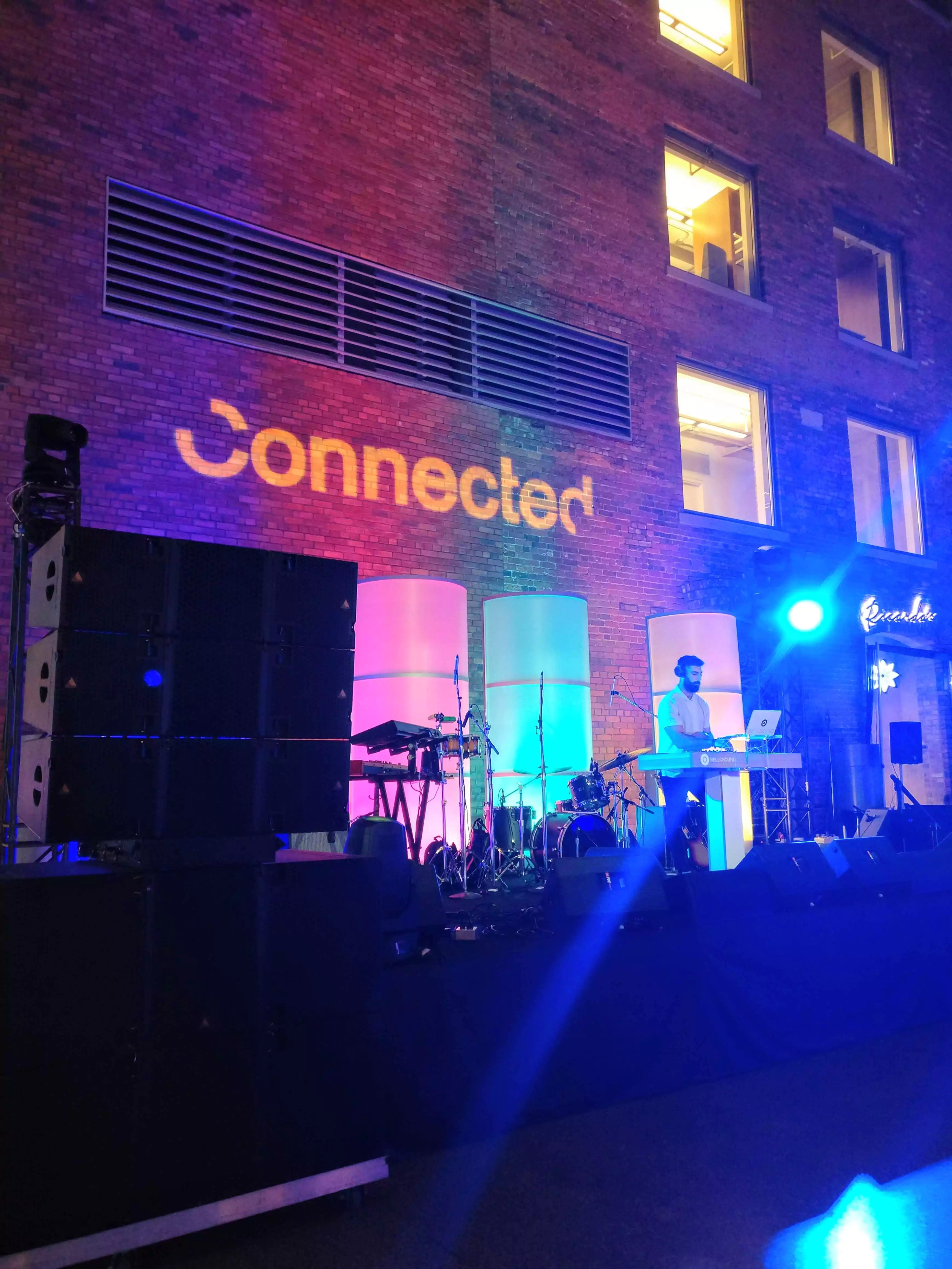 DJ standing in front of a wall backlit with the Connected logo
