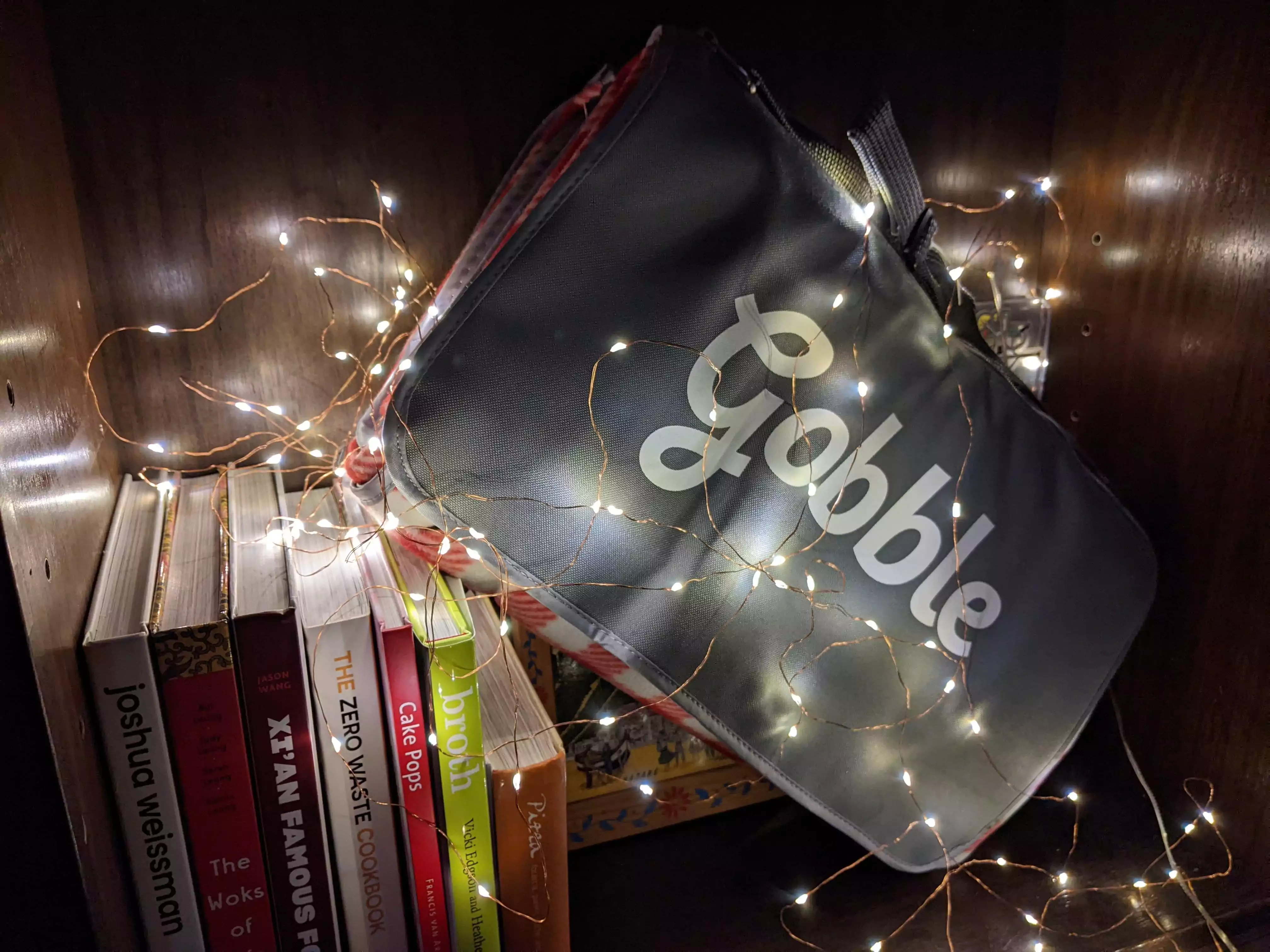 Folded up picnic blanket with the Gobble logo, sitting on cookbooks and covered in string lights