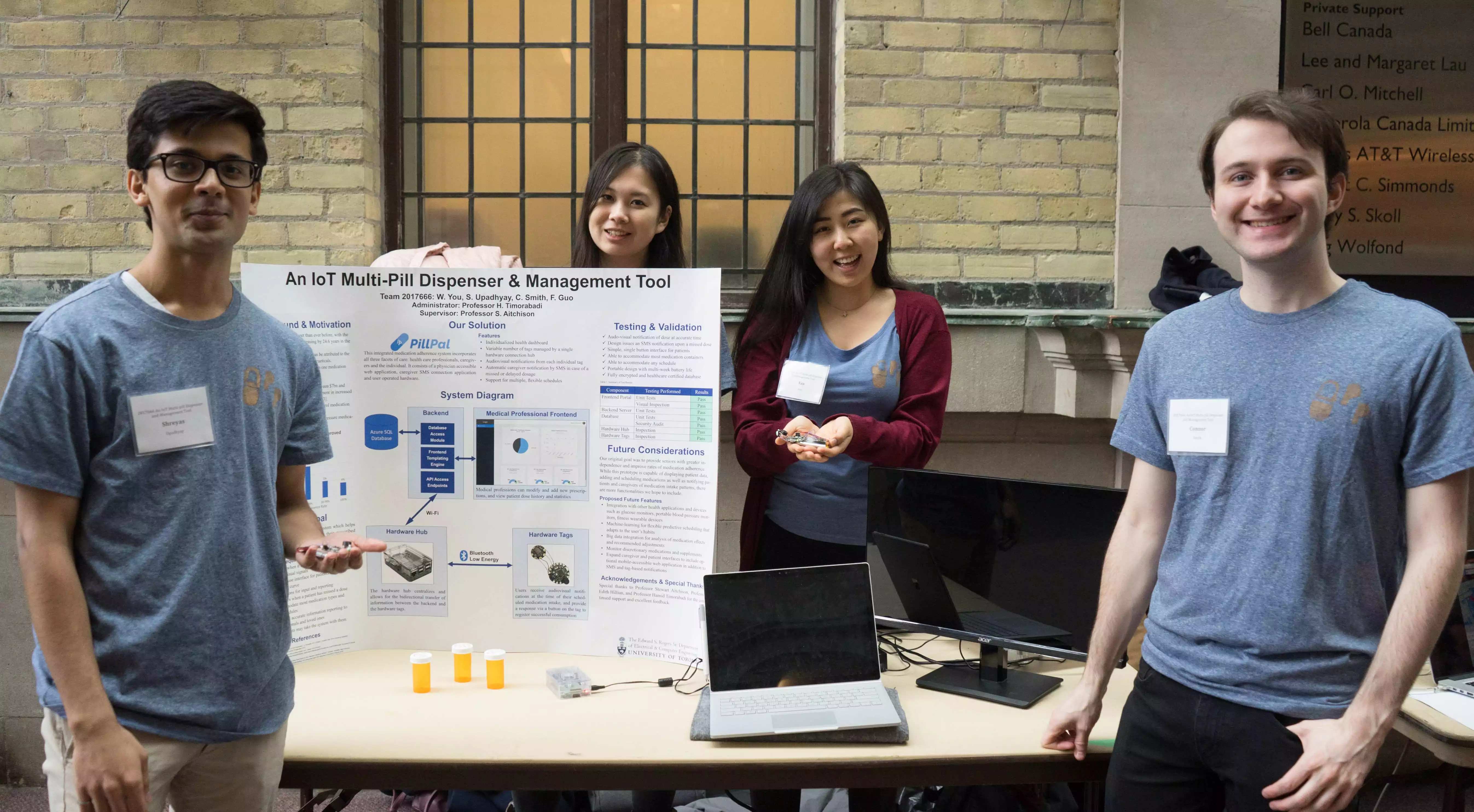 Four students smiling and standing with a project board titled 'An IOT Multi-Pill Dispenser and Management Tool'